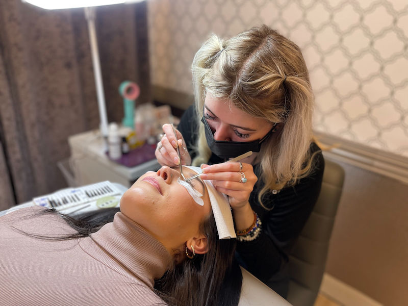 woman lying down getting lash extensions by a stylist